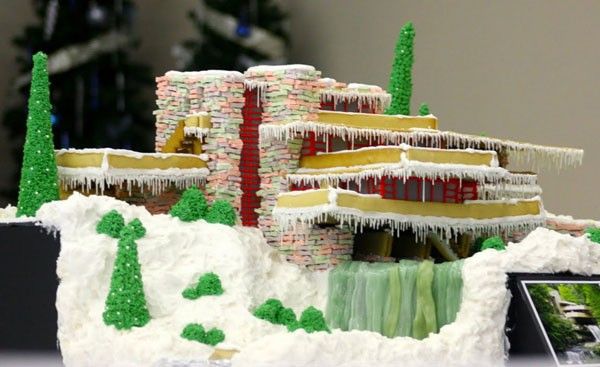 a gingerbread house with icing on the roof and trees in front of it