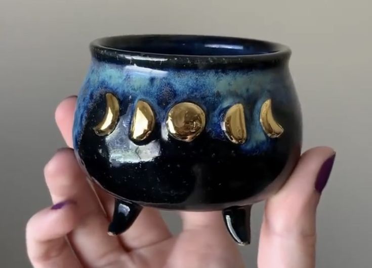 a hand holding a blue and black cup with gold decorations on the outside of it