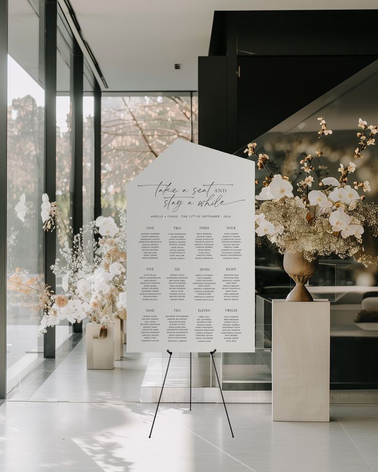 a white sign sitting on top of a floor next to vases filled with flowers