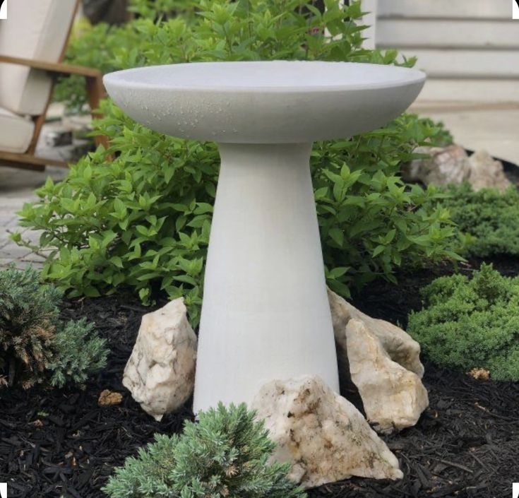 a white bird bath surrounded by plants and rocks