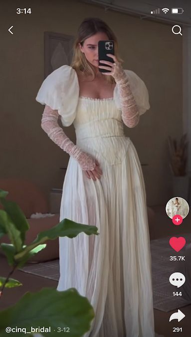 a woman in a white dress is taking a selfie with her cell phone while wearing gloves