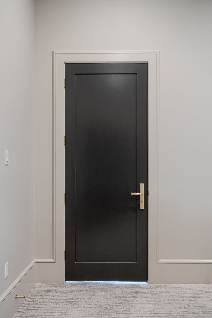 an empty room with a black door and white walls, carpeted flooring on the ground