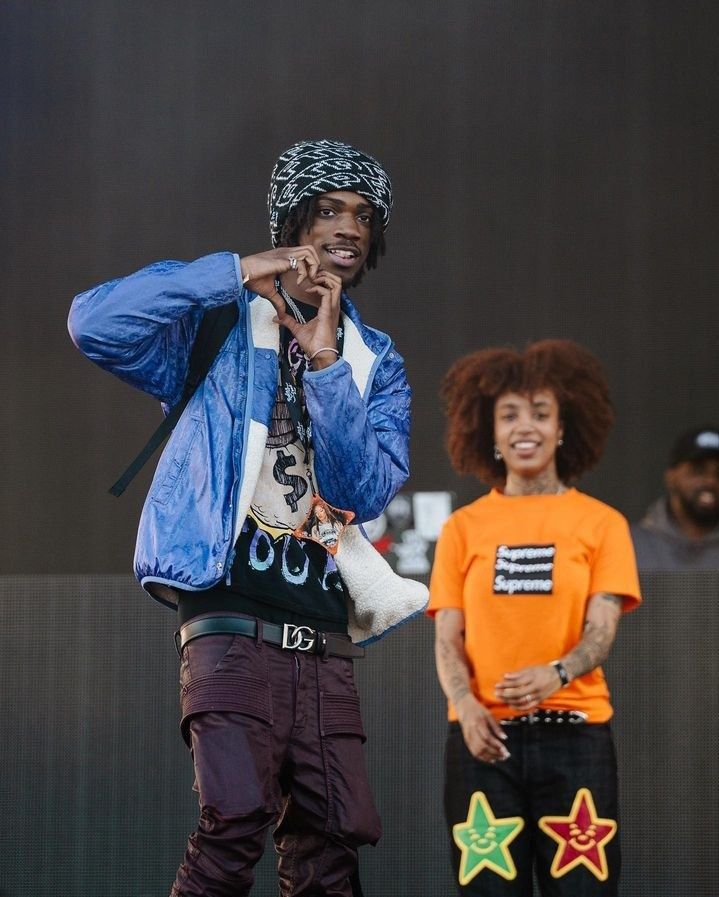 two young men standing on stage with one holding his hand up to his ear and the other wearing an afro wig