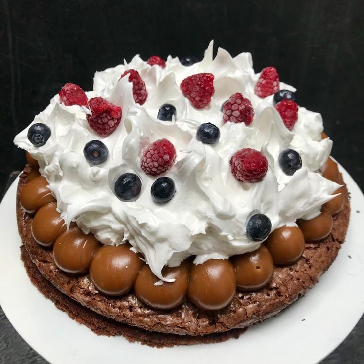 a chocolate cake topped with whipped cream, berries and other toppings on a white plate