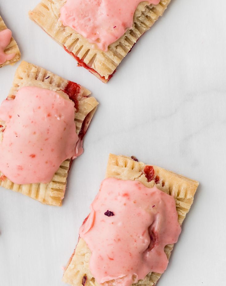 four desserts with pink icing and cranberries on them sitting on a white surface