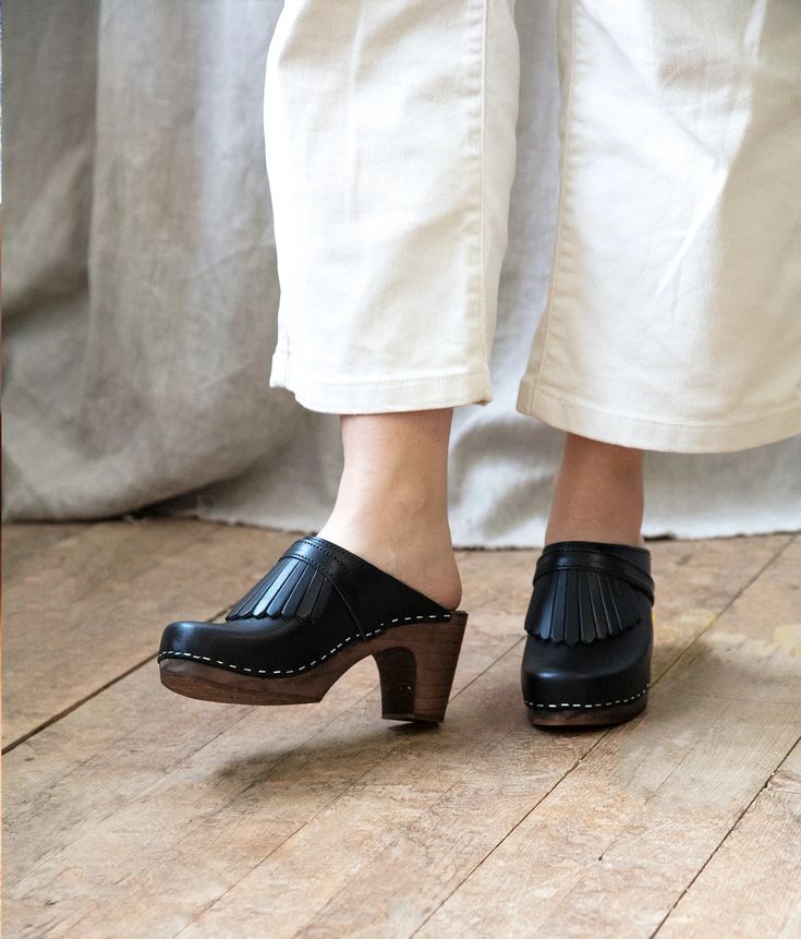 Add a touch of playful elegance with the Venice clog mules by Sandgrens. These open back and fringed clog mules boast a refreshing take on a timeless design, ideal for professional settings that demand an elevated yet fun aesthetic. With handcrafted construction and premium quality materials, the Venice are not only stylish but durable enough to withstand daily wear. Clog measurements:Heel height: 3 1/8'' (8 cm)Toe height: 1 1/4'' (3.2 cm) Fit:NarrowLeather:Vegetable tanned leatherClogs consist Sandgrens Clogs, Clog Mules, Fun Aesthetic, Clogs For Women, Black Clogs, Clog Boots, Cork Sandals, Wooden Clogs, Heel Mules