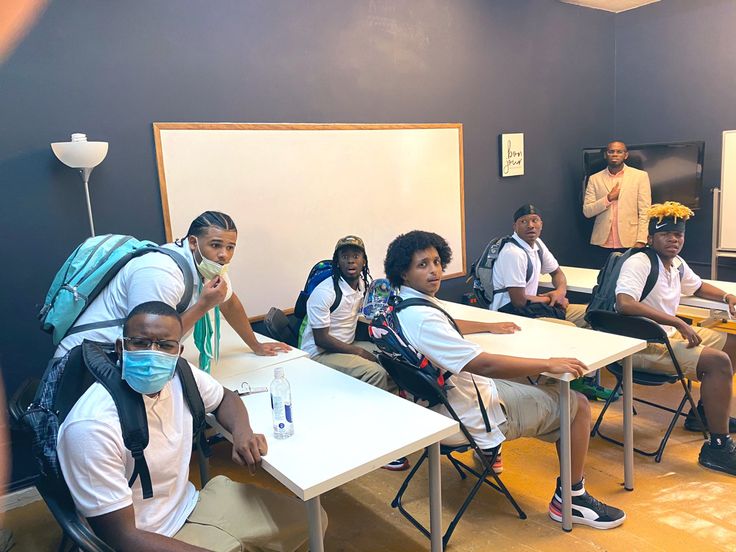 a group of young people sitting at desks with masks on their faces and wearing backpacks