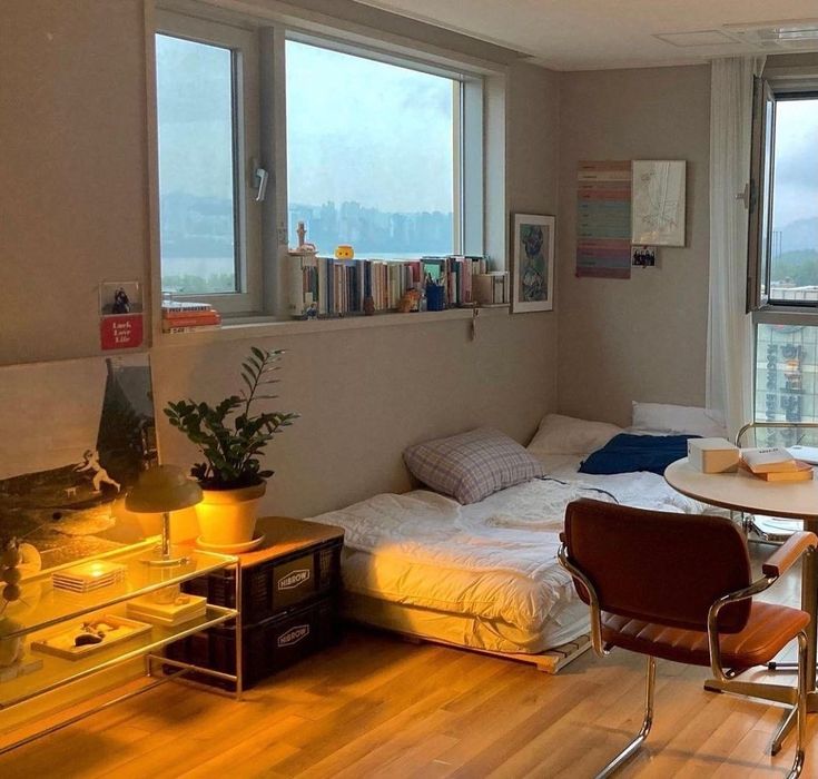 a bedroom with a bed, desk and window overlooking the cityscape in the distance