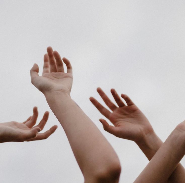 four hands reaching up into the air to catch a frisbee