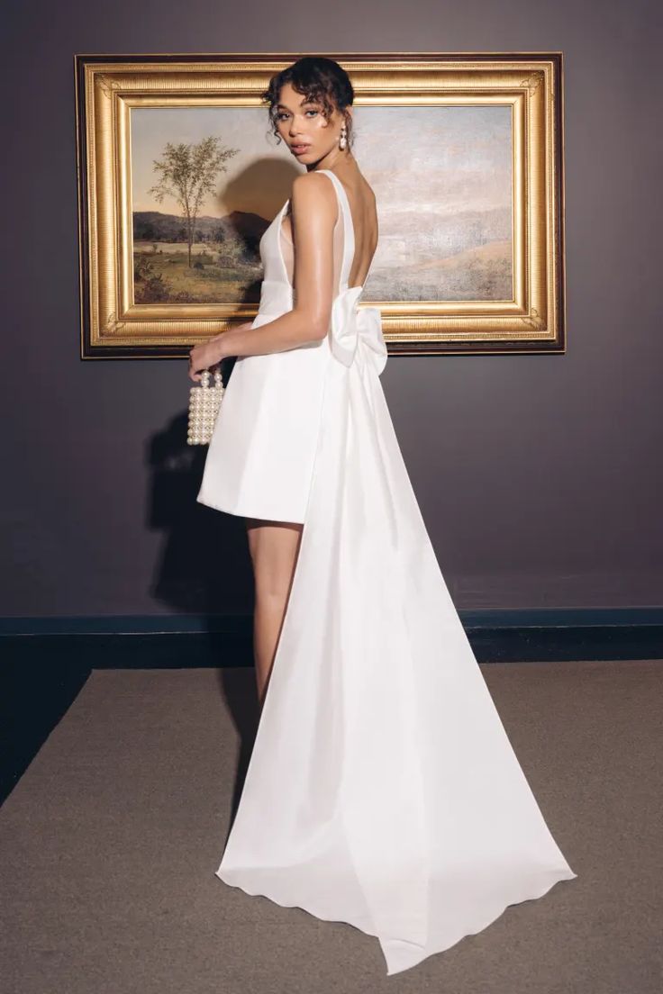 a woman standing in front of a painting wearing a white dress with high slits