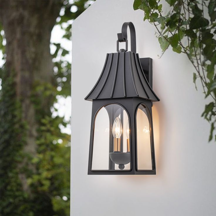 an outdoor wall light with two lights attached to it's side and trees in the background