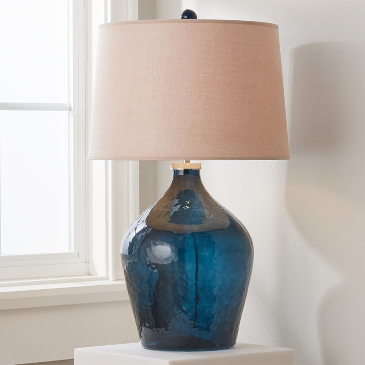 a blue vase sitting on top of a white table next to a lamp with a beige shade