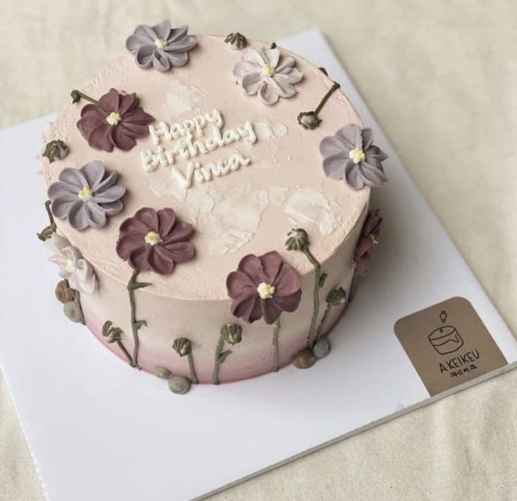 a pink birthday cake with purple flowers on it