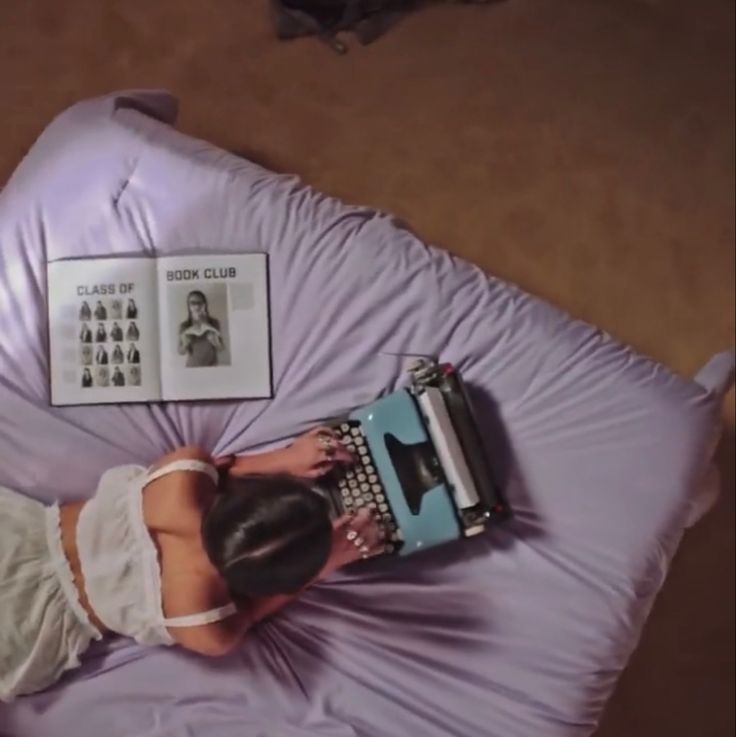 a woman laying on top of a bed with an old typewriter in her hand