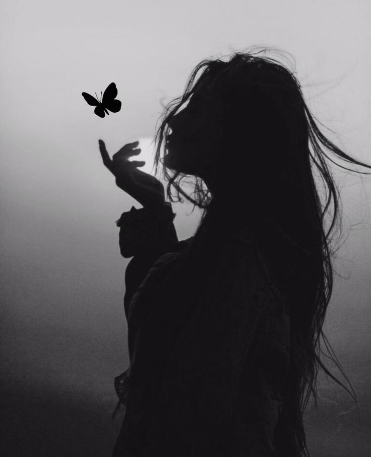 a black and white photo of a woman with long hair holding a butterfly in her hand