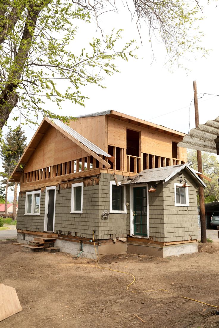 a house being built in the middle of a dirt lot next to a large tree