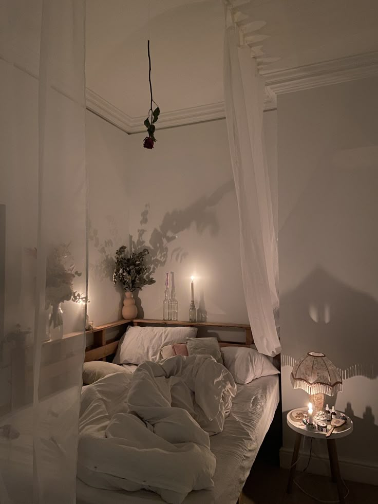 an unmade bed in a white room with candles on the nightstands and curtains