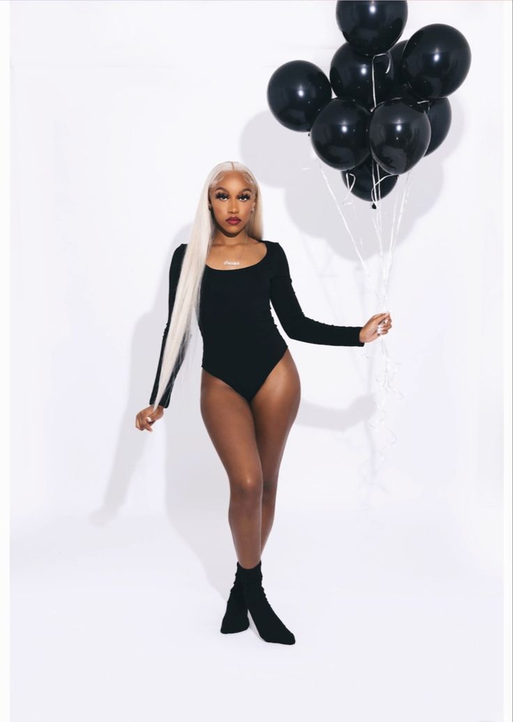 a woman in a black bodysuit holding balloons and posing for the camera with her legs crossed