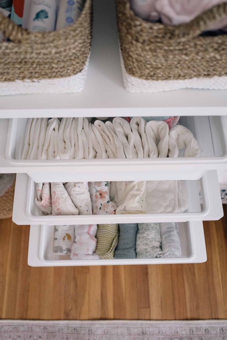 an organized drawer with baby clothes and diapers in the bottom shelf, on top of a wooden floor