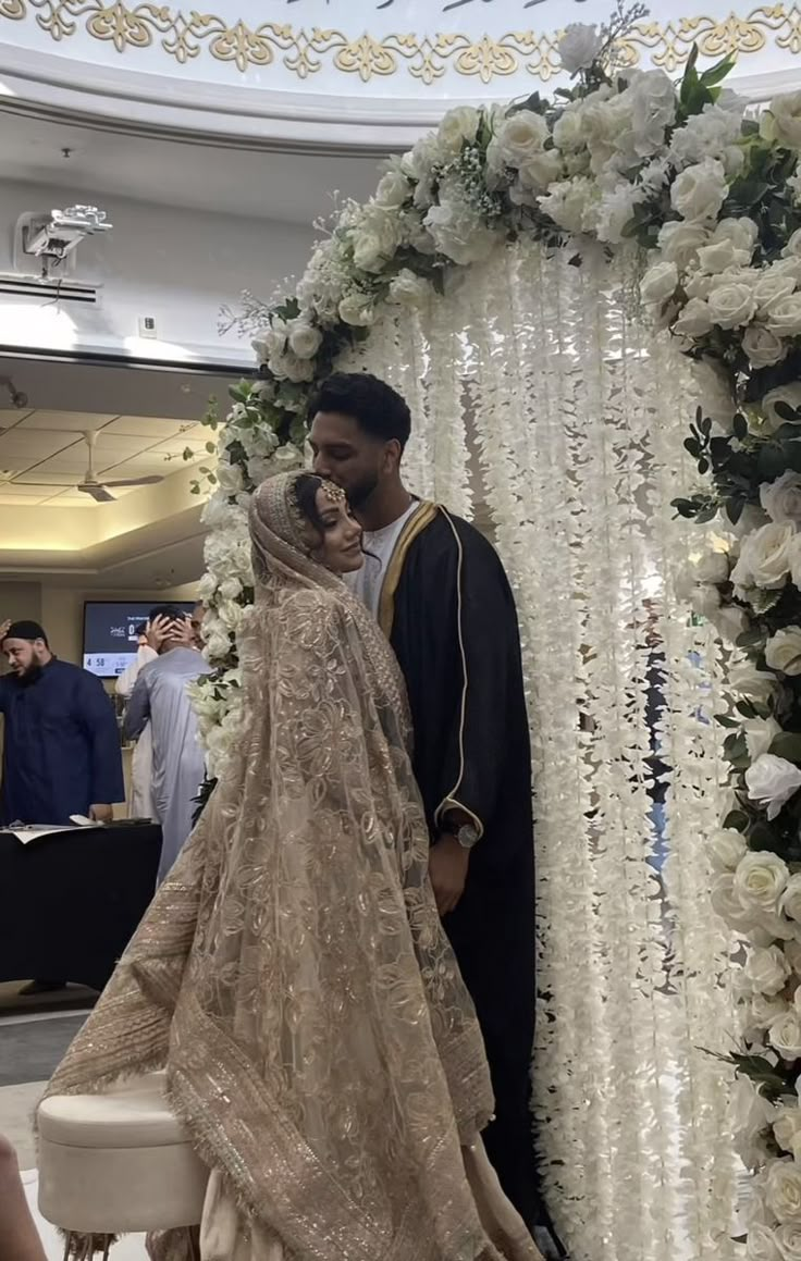 a man and woman standing next to each other in front of a flower covered arch