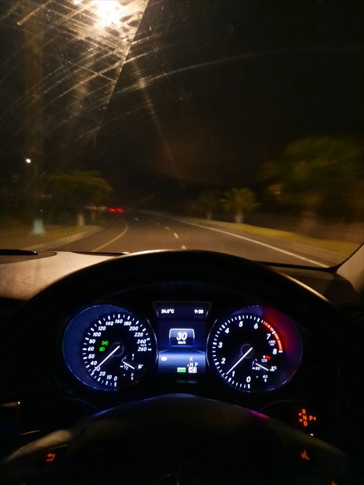 the dashboard of a car at night with lights on and streetlights in the background