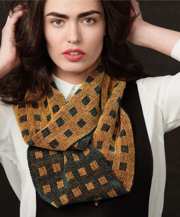 a woman is wearing a scarf with black and yellow squares on it, while she has her hands behind her head