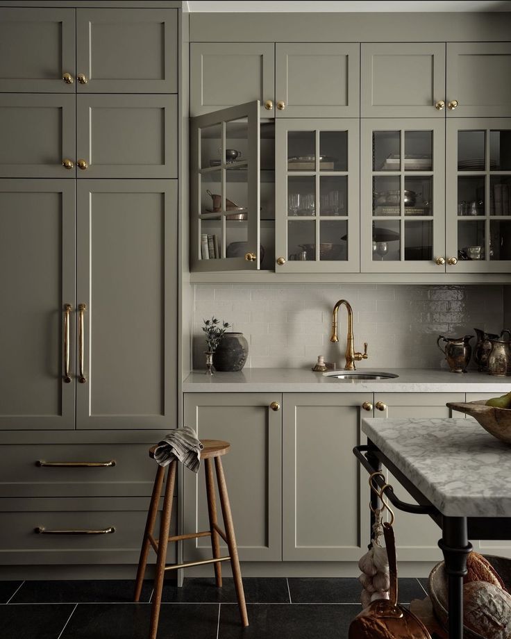 a kitchen with gray cabinets and marble counter tops, gold handles and brass pulls on the doors