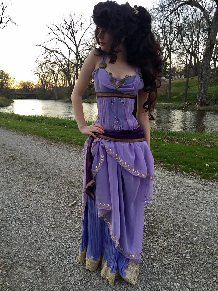 a woman in a purple dress is standing on the gravel near some trees and water