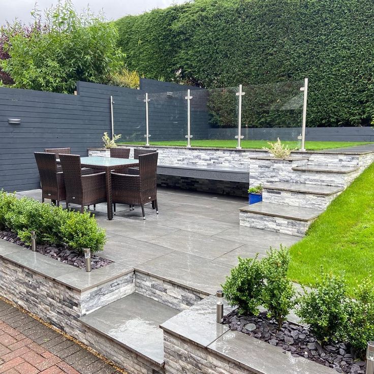 an outdoor patio with steps leading up to the dining table and seating area, surrounded by greenery