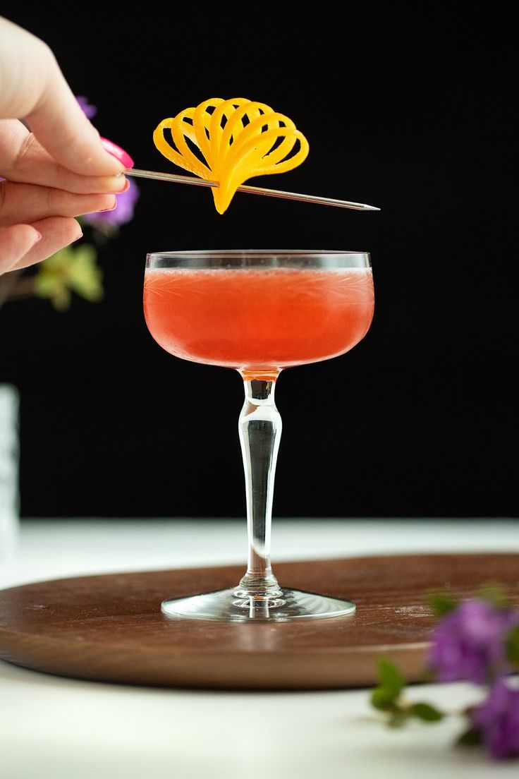 a person is holding a yellow flower in a wine glass with a drink on the side