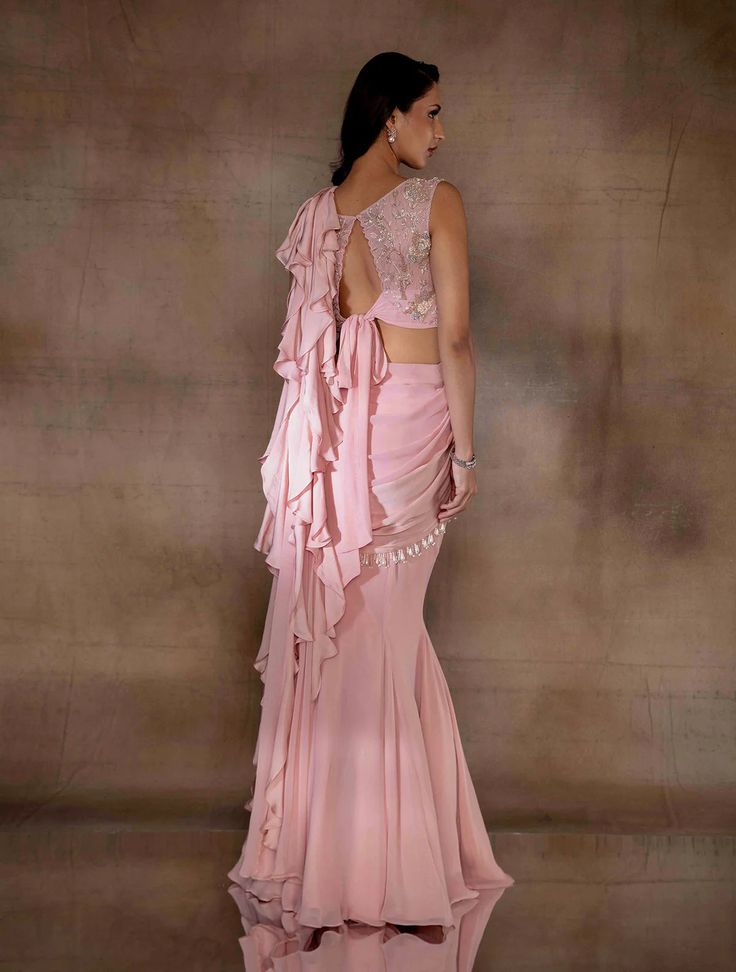 Soft pink fishtial sari with an attached georgette & satin georgette pallu hand embellished with dangling glass bugles & ivory pearls, with a satin georgette ruffle pallu. Paired with a corset crop hand embellished with champagne florals & an open embellished tie back.From Shloka Khialani's Winter Sun collection.DELIVERY TIMEPlease allow 6-8 weeks for your outfit to arrive.FABRIC DETAILSGeorgette, Satin Georgette, Net, CrepeProfessional cleaning only. Floor-length Ruffled Saree For Reception, Silk Saree With Ruffles For Evening, Festive Ruffled Silk Saree, Evening Sharara With Ruffles And Traditional Drape, Evening Silk Lehenga With Ruffles, Silk Lehenga With Ruffles For Evening, Designer Georgette Pre-draped Saree With Ruffles, Silk Pre-draped Saree With Ruffles For Wedding, Pink Pre-draped Saree With Ruffles For Wedding