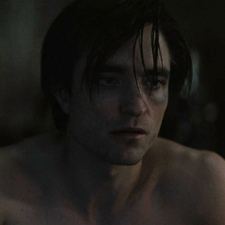 a shirtless young man stares at the camera in a dark room with only his chest visible