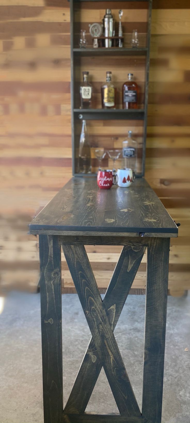 a wooden table sitting in front of a shelf with bottles on top of it next to a wall