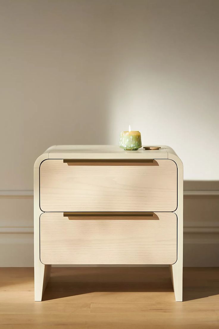 a white nightstand with a green vase sitting on it's top and bottom drawer