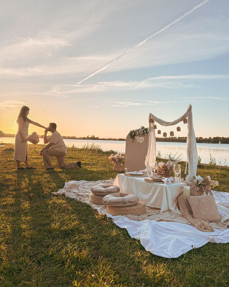 two people setting up an outdoor table on the grass near water at sunset or dawn