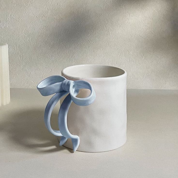 a white cup with a blue bow on the side sitting next to a small book