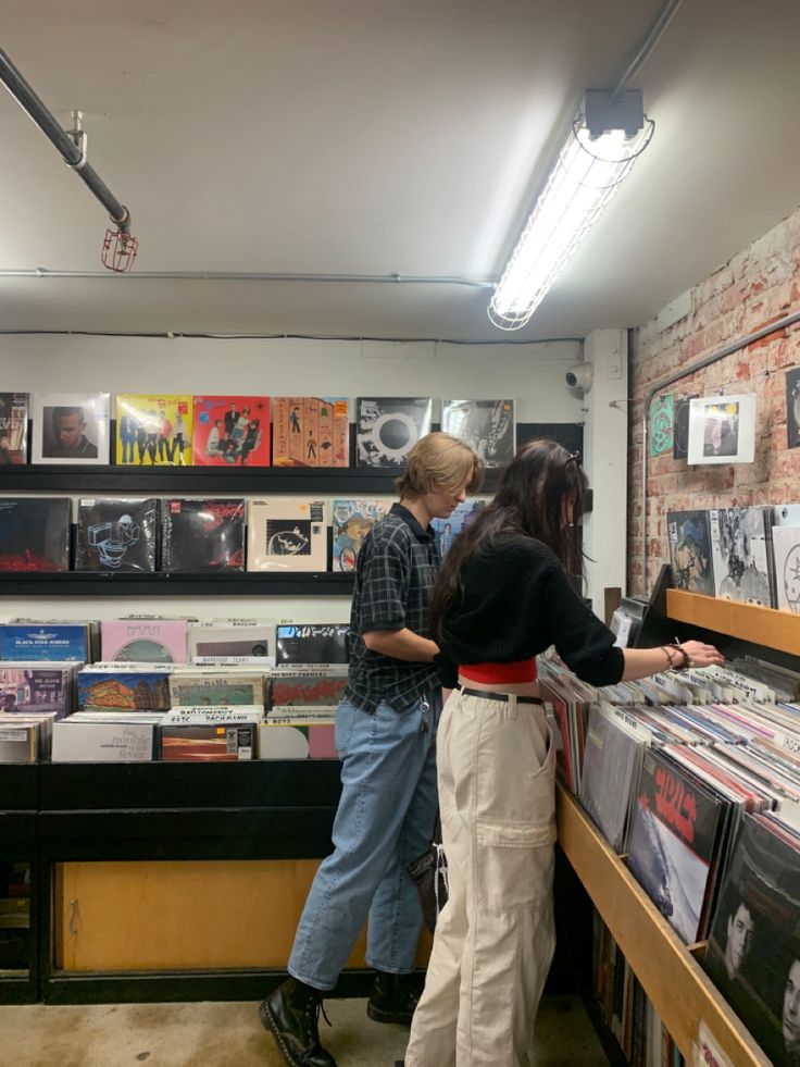 two people looking at records on display in a music store with brick walls and exposed lighting