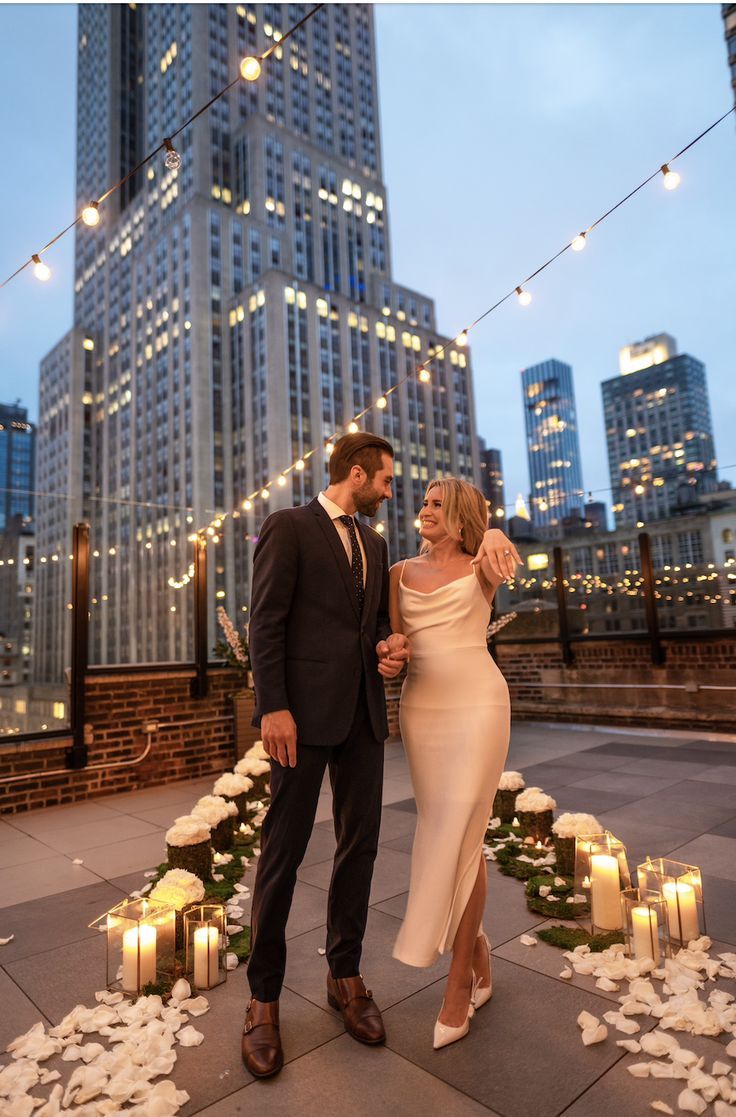 a man and woman standing next to each other in front of tall buildings at night