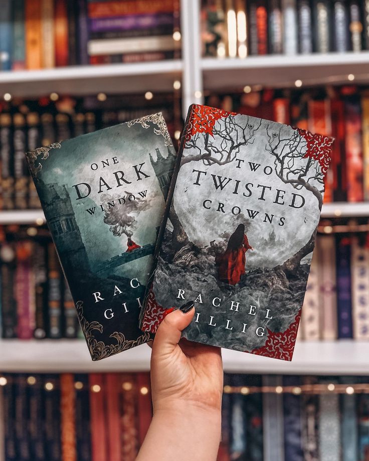 two books in front of a book shelf with many books on it and one being held up by a hand