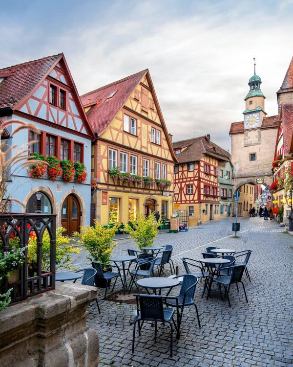 an old european town has tables and chairs on the cobblestone street with flowers in pots