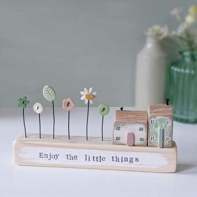 a small wooden house with flowers in the front and an inscription on the back that says enjoy the little things