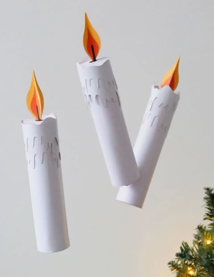 two white candles with orange flames on them next to a christmas tree ornament