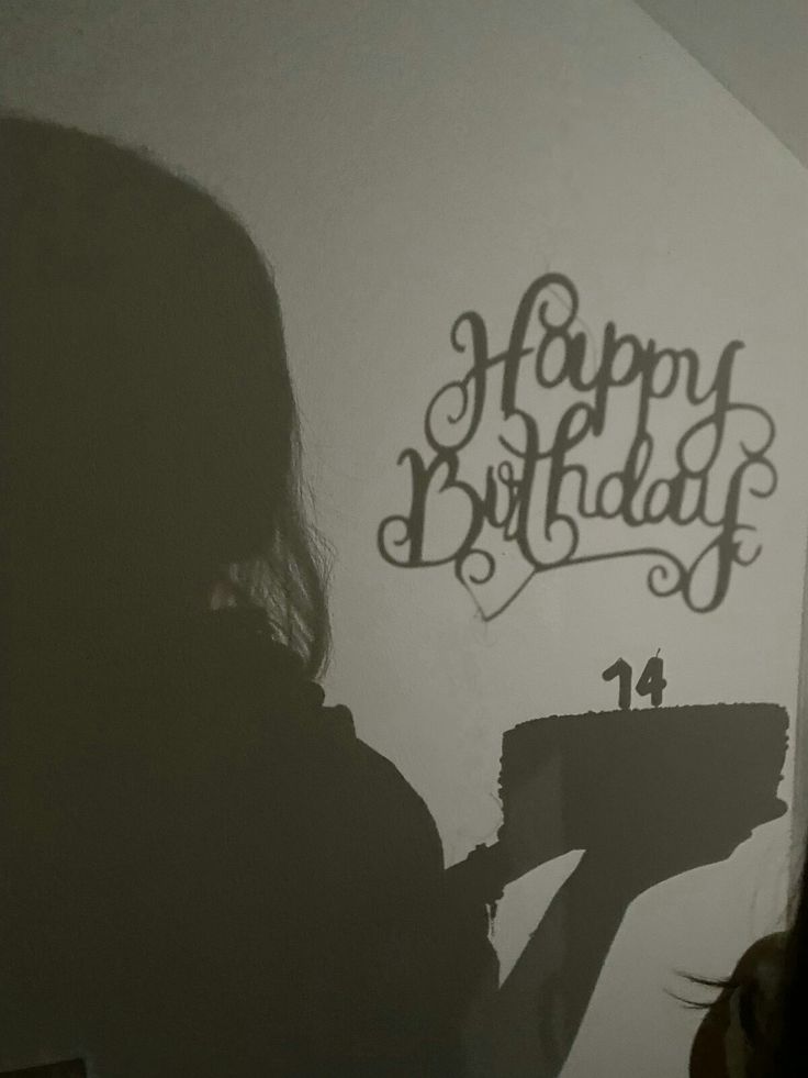 the shadow of a woman holding a paintbrush in front of a wall with happy birthday written on it