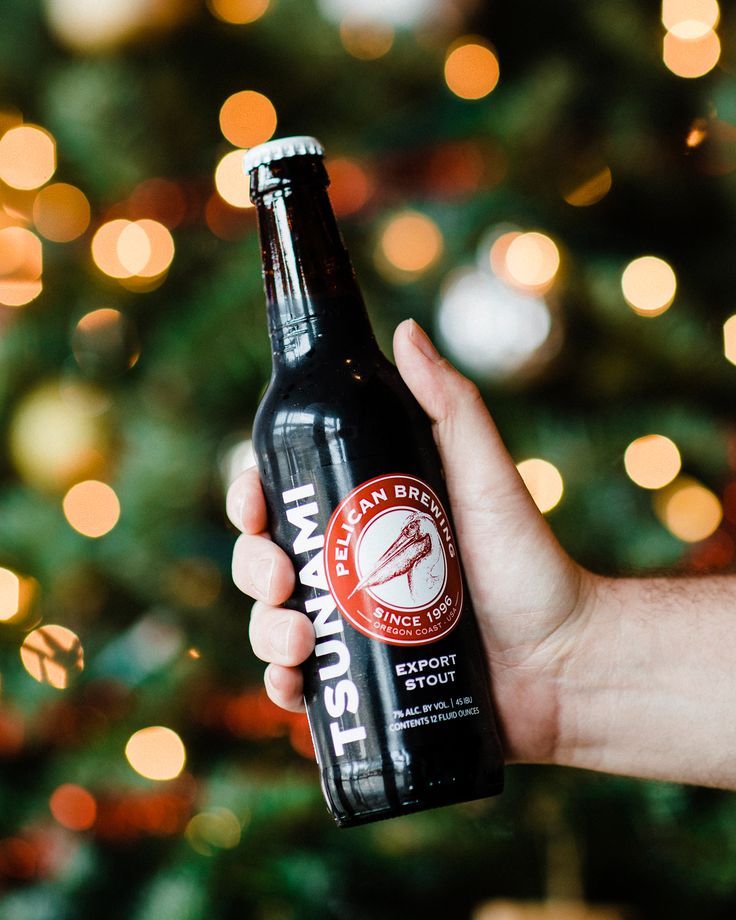 a person holding up a beer in front of a christmas tree