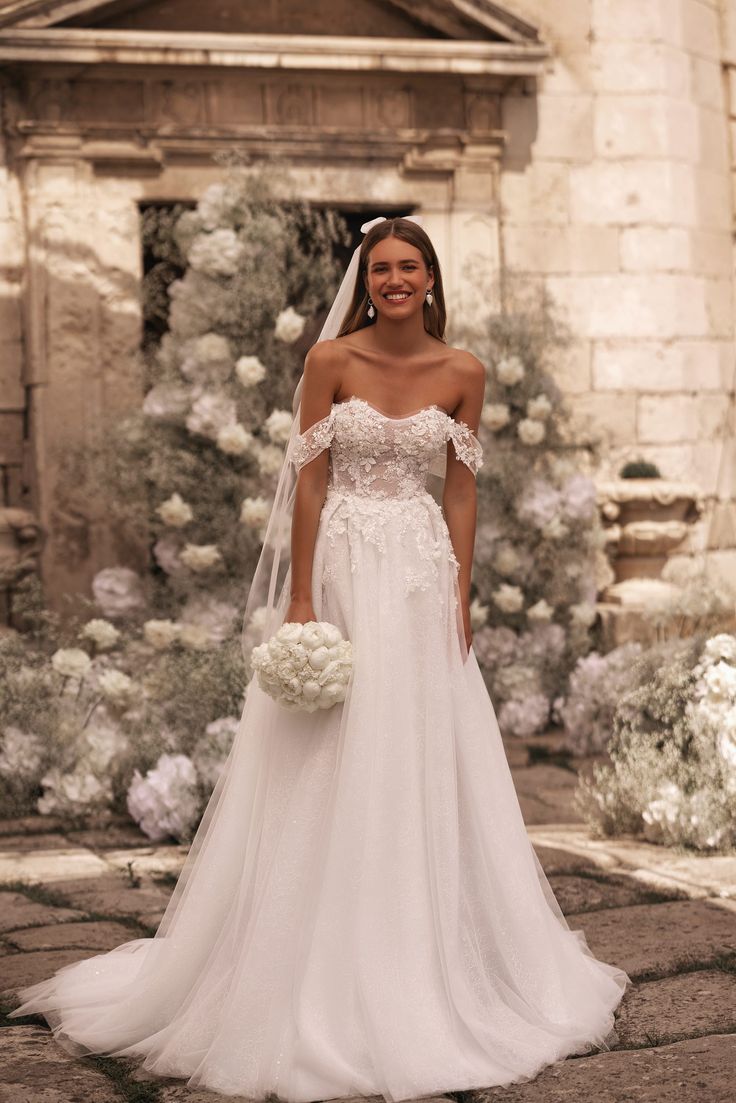 a woman in a wedding dress posing for the camera with white flowers around her neck