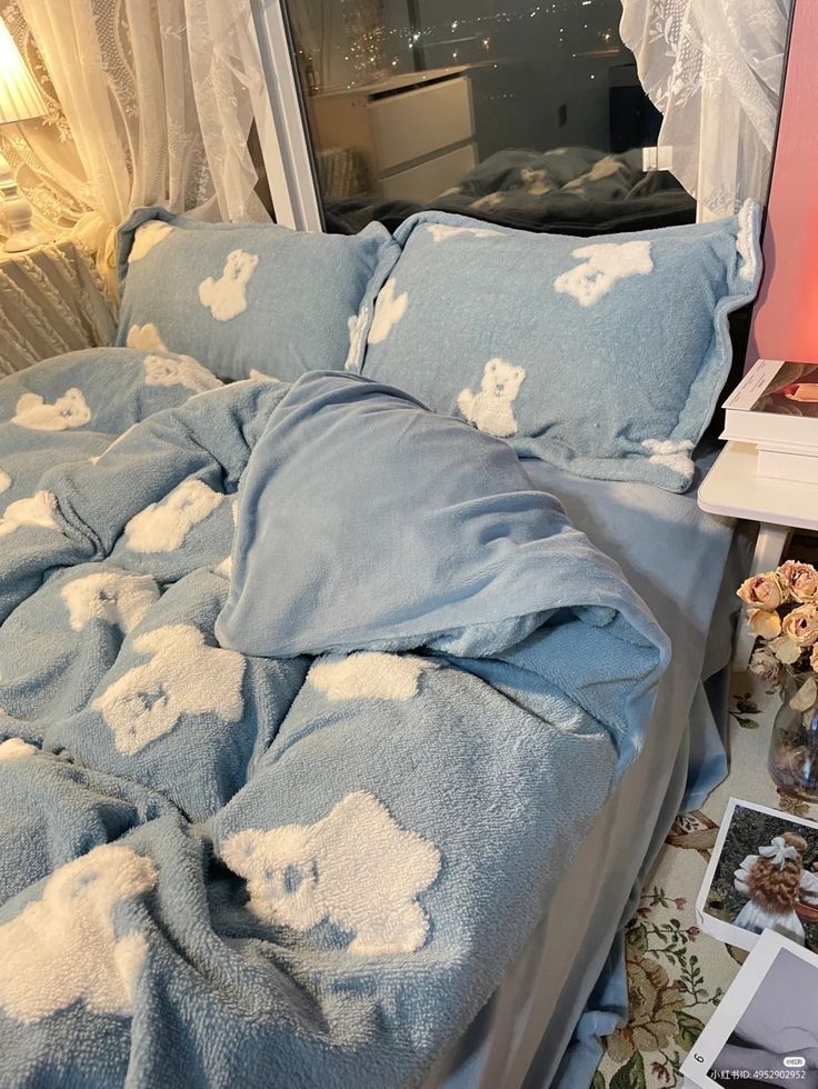 an unmade bed with blue and white teddy bears on the comforter in front of a window