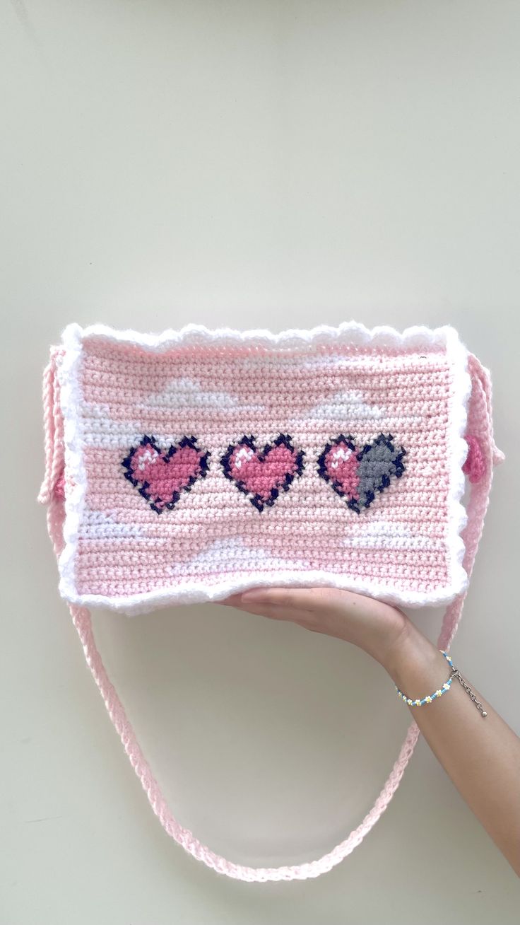 a hand holding a pink crocheted purse with hearts on it