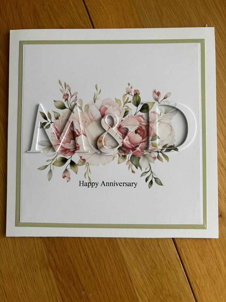 an anniversary card with flowers and the word m & w on it, sitting on a wooden surface