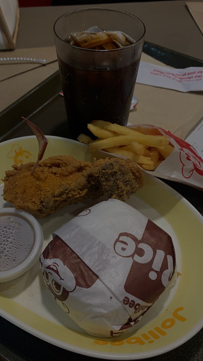 a plate with some food on it next to a glass of soda and french fries