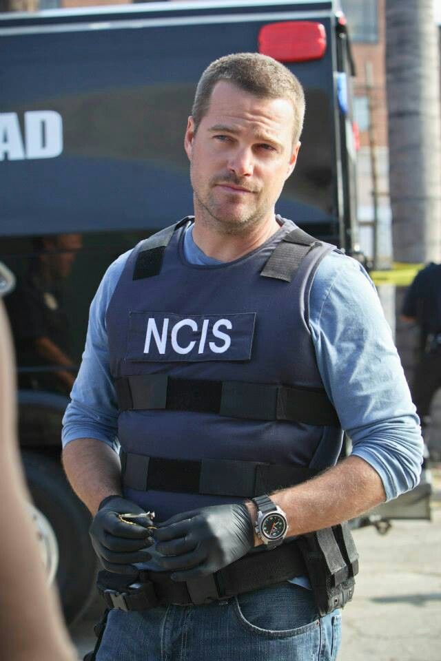 a man in a police uniform standing next to a black truck with the words ncis on it